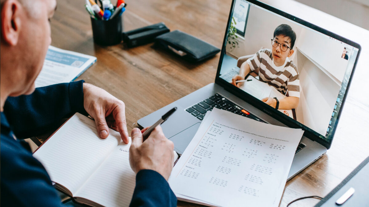 young asian boy visible on laptop screen as a teachers writes notes